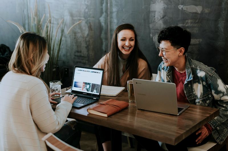 Young team members laughing together while planning around a table with laptops
