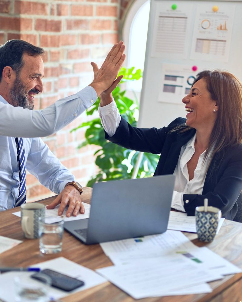 Two coworkers sharing a high five across a desk after a successful day